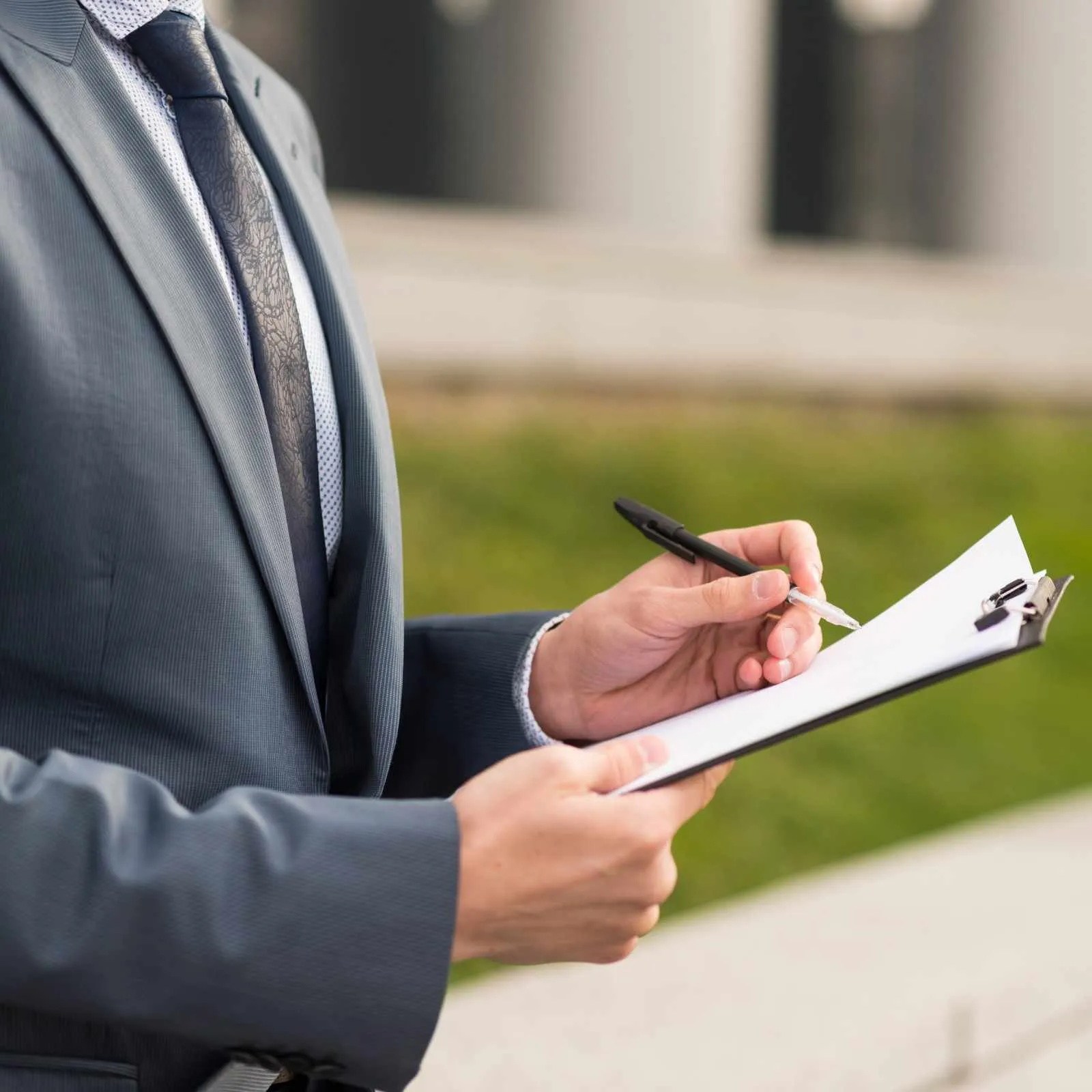Person in a suit writing notes on a clipboard outdoors
