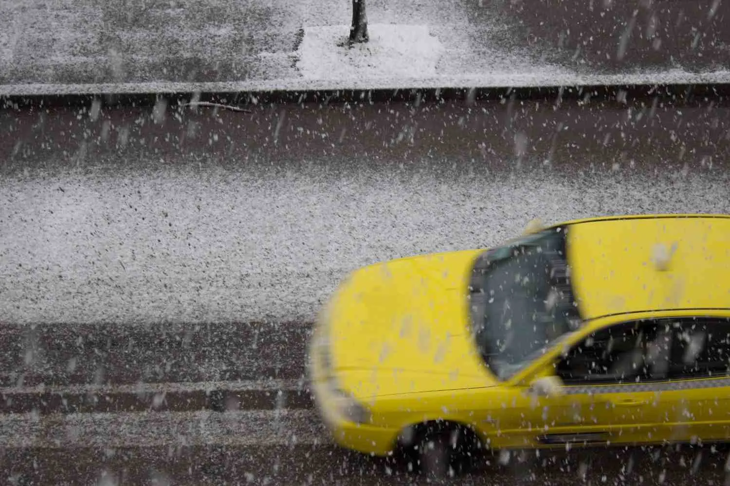 Yellow car driving down a snowy street during a winter storm